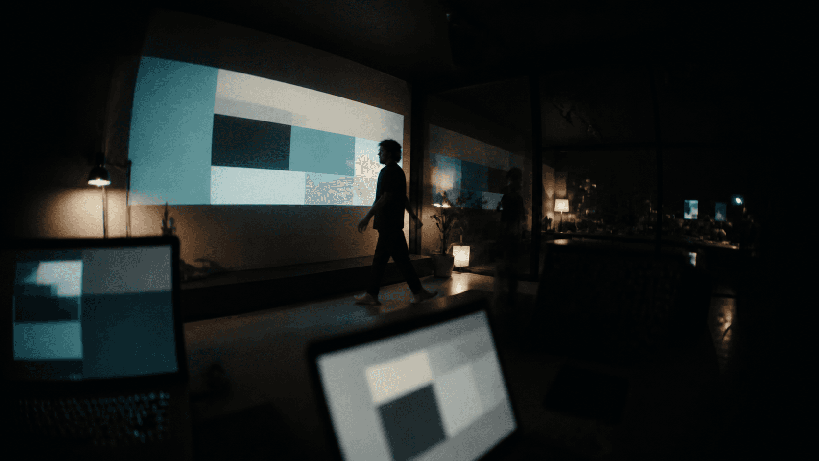 A designer moving through a dark studio filled with projected digital compositions